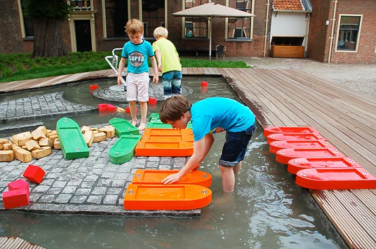 Kinderen laten boten varen en bedienen de speelelementen van de waterbaan.